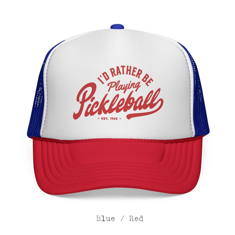 Puede incluir: Gorra de camionero roja, blanca y azul con el texto "I'D RATHER BE PLAYING PICKLEBALL - EST. 1965" en escritura roja. La gorra tiene una visera roja, un panel frontal blanco y una parte trasera de malla azul. Un bot&oacute;n azul est&aacute; en la parte superior.