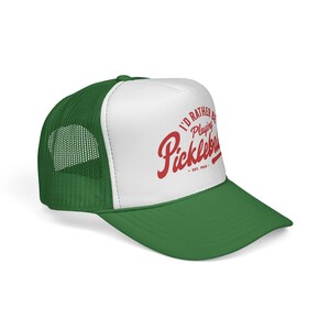 Puede incluir: Gorra de camionero verde y blanca con el texto "I'd Rather Be Playing Pickleball" en escritura roja. La gorra tiene una visera y una parte trasera de malla verdes, y un panel frontal blanco. El texto incluye "Est. 1965".