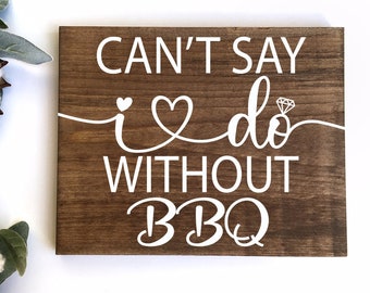 May include: A brown wooden sign with white text that reads "Can't say I do without BBQ". The text includes a heart with a diamond ring inside.