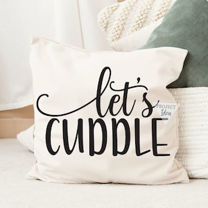 Könnte beinhalten: Ein weißes Kissen mit schwarzem Text, der "let's cuddle" lautet. Das Kissen liegt auf einer weißen Oberfläche mit einem grünen Überwurfkissen und einem weißen Häkelkissen dahinter.