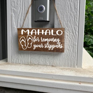 May include: A wooden sign with the text "Mahalo for removing your slippers" in white lettering. The sign also features a pair of flip-flops in white.
