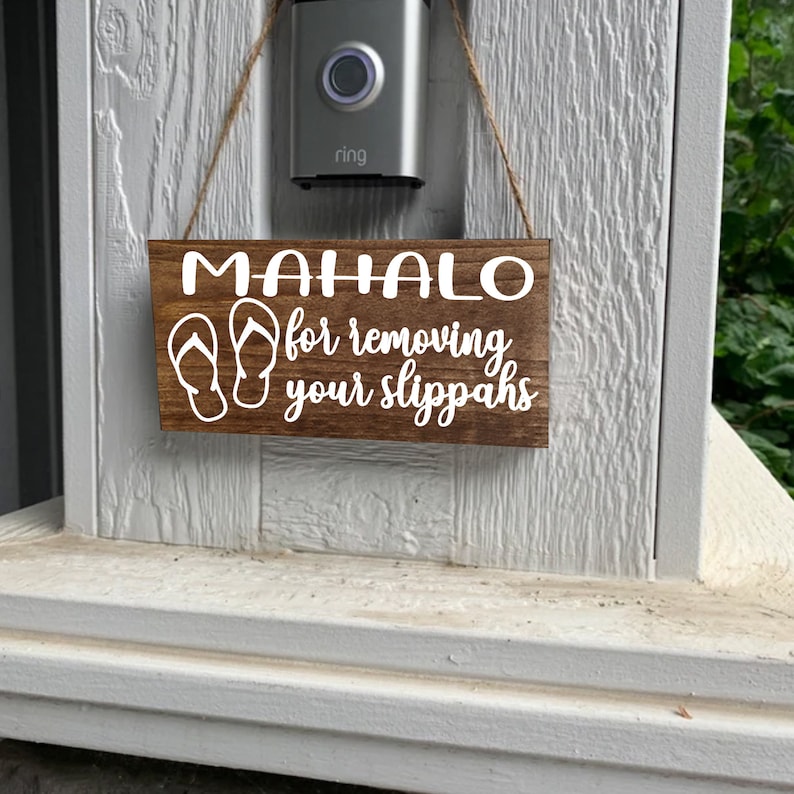 May include: A wooden sign with the text "Mahalo for removing your slippers" in white lettering. The sign also features a pair of flip-flops in white.