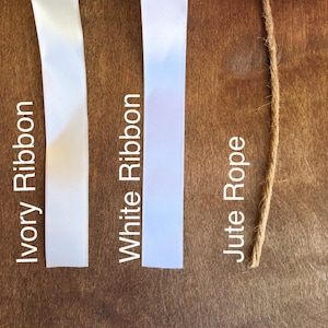 May include: Close-up of three different types of ribbon and rope.  Ivory ribbon, white ribbon, and jute rope.