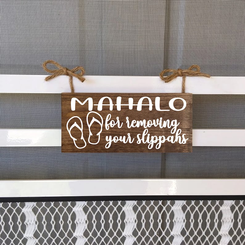 May include: A wooden sign with the text "MAHALO for removing your slippers" in white lettering. The sign is hanging from a white door frame with twine.