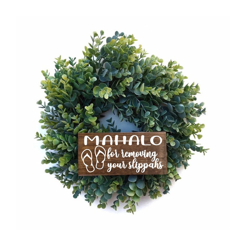 May include: A wooden sign with the text "Mahalo for removing your slippers" and a graphic of flip flops hangs on a green wreath.