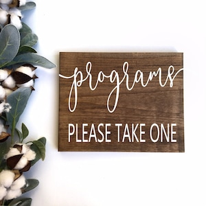 May include: A rustic wooden sign with white text that reads "programs please take one".