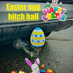 Może przedstawiać: Kula haka holowniczego w tematyce jaj wielkanocnych z niebiesko-żółtym wzorem jajka. Obraz zawiera tekst "Easter egg hitch ball" oraz grafikę "Happy Easter" z królikiem i kolorowymi jajkami.