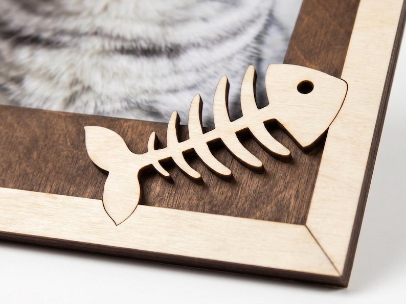May include: A wooden picture frame featuring a two-tone design with a dark brown inner border and a light beige outer border. A light-colored wooden cutout of a fish skeleton is attached to the corner of the frame.