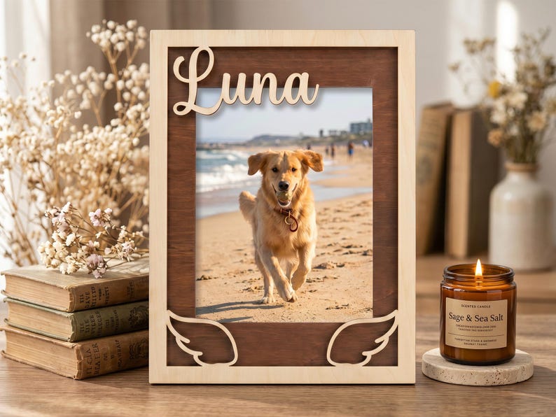 May include: A rectangular wooden picture frame with a light wood outer border and a dark wood inner frame. The top features the name Luna in script, and the bottom corners have carved angel wing designs. It holds a photo of a golden dog.