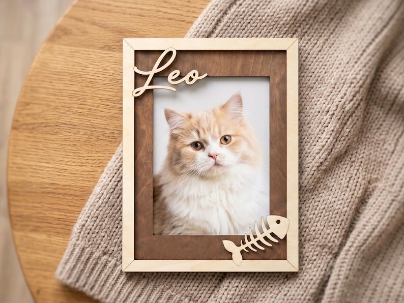 May include: A rectangular wooden picture frame with a dark brown inner border and a light wood outer frame. The name Leo is cut out in light wood at the top left, and a fish skeleton shape is attached at the bottom right corner.