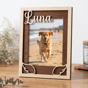 May include: A rectangular wooden picture frame with a dark brown inner border and a light natural wood outer border. The top features the name Luna in cursive script, and the bottom corners have cutout angel wing designs.