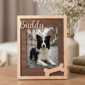 May include: A rectangular wooden picture frame with a light-colored outer border and a dark wood inner panel. The frame features the word Buddy in script lettering at the top and a bone-shaped cutout at the bottom right corner.