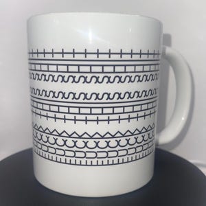 Könnte beinhalten: Weiße Keramiktasse mit einem schwarzen geometrischen Muster. Das Design zeigt horizontale Bänder aus Linien, Zickzacklinien und Kurven. Die Tasse hat einen gebogenen Griff und ist für heiße oder kalte Getränke geeignet.
