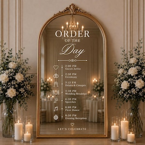 Op de afbeelding: Een boogvormige vloerspiegel met een gouden lijst met witte tekst die ORDER OF THE DAY leest, gevolgd door een trouwschema met iconen en tijden van 14:00 tot 20:30 uur, eindigend met de tekst LET'S CELEBRATE onderaan.