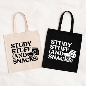 May include: Two tote bags, one cream and one black, with the text "STUDY STUFF (AND SNACKS)" in bold white lettering. The design includes a book and a snack container. The bags have handles for carrying.