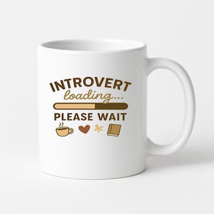 Puede incluir: Taza de cerámica blanca con el texto "INTROVERT loading... PLEASE WAIT" en letras marrones. La taza presenta una barra de carga, una taza de café, un corazón, una flor y un icono de libro. La taza tiene un asa curva.