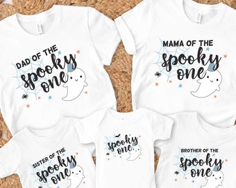 May include: Set of five white t-shirts with a Halloween theme. The shirts feature a ghost with a party hat and the text "Dad of the spooky one", "Mama of the spooky one", "Sister of the spooky one", "Brother of the spooky one", and "Spooky one".