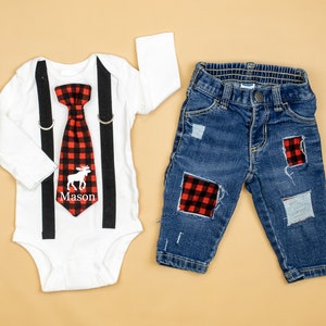May include: A white bodysuit with black suspenders and a red and black plaid bow tie with a white moose and the name "Mason" embroidered on it. The bodysuit is paired with blue denim jeans with red and black plaid patches.