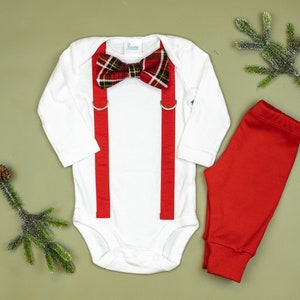 May include: A white long-sleeve bodysuit with red suspenders and a plaid bow tie. The outfit is paired with red pants.