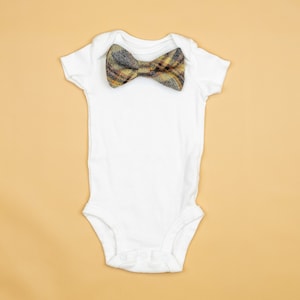 May include: A white baby onesie with a brown and yellow plaid bow tie.