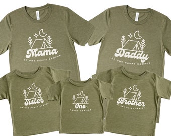 May include: Set of five green t-shirts with a camping theme. The shirts feature a white outline of a tent, moon, and stars with the text "Mama of one happy camper", "Daddy of one happy camper", "Sister of one happy camper", "Brother of one happy camper", and "One happy camper".