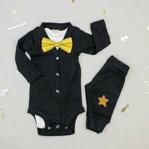 Puede incluir: Un body negro con una pajarita dorada y pantalones negros a juego con una estrella dorada. El atuendo es perfecto para el primer cumplea&ntilde;os de un beb&eacute; o una ocasi&oacute;n especial.