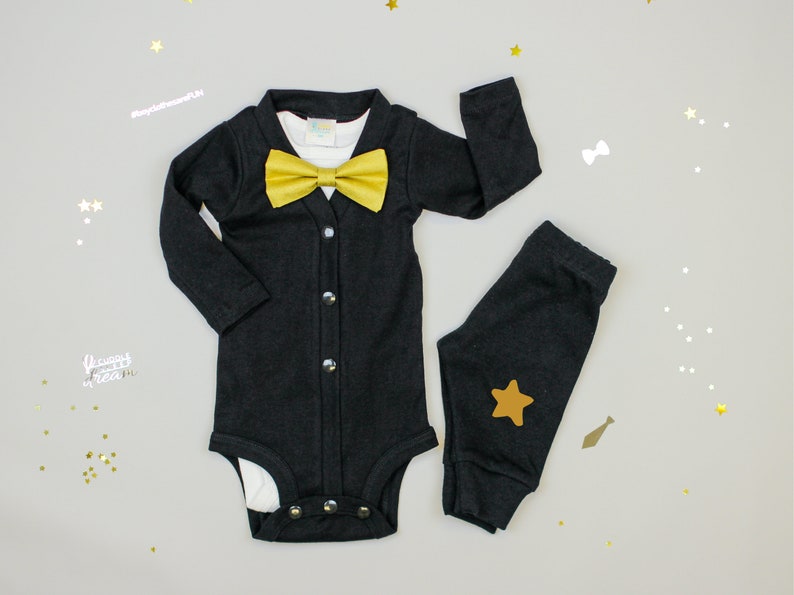 Puede incluir: Un body negro con una pajarita dorada y pantalones negros a juego con una estrella dorada. El atuendo es perfecto para el primer cumplea&ntilde;os de un beb&eacute; o una ocasi&oacute;n especial.