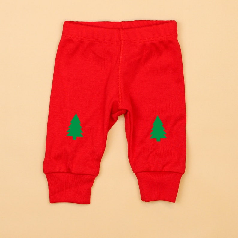 May include: Red baby leggings with green Christmas tree designs on the knees.