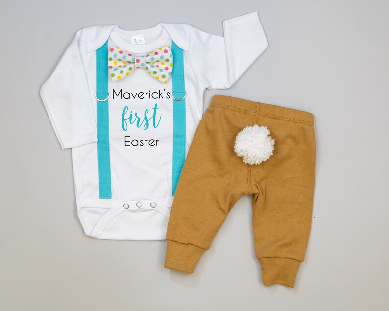 Puede incluir: Mono blanco de manga larga con tirantes turquesa y una pajarita de lunares multicolores. El mono tiene el texto "Maverick's first Easter" impreso. Pantal&oacute;n marr&oacute;n con una cola de pomp&oacute;n blanco.