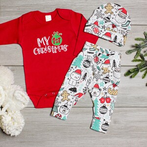 May include: Red long-sleeve onesie with "My 1st Christmas" text, white and green Christmas-themed leggings, and a white hat with a gingerbread man and Santa Claus design.
