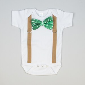 May include: A white baby onesie with brown suspenders and a green bow tie with a tropical leaf pattern.