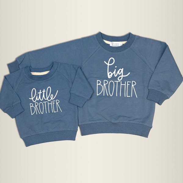 Puede incluir: Dos sudaderas azules, una más pequeña que la otra. La sudadera más pequeña dice "little brother" en escritura blanca, y la más grande "big brother". Ambas tienen cuello redondo y mangas largas.