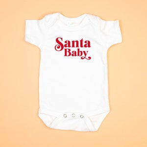 May include: White baby onesie with red text that says "Santa Baby".