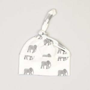 May include: White baby hat with a grey elephant print and a knot on top.