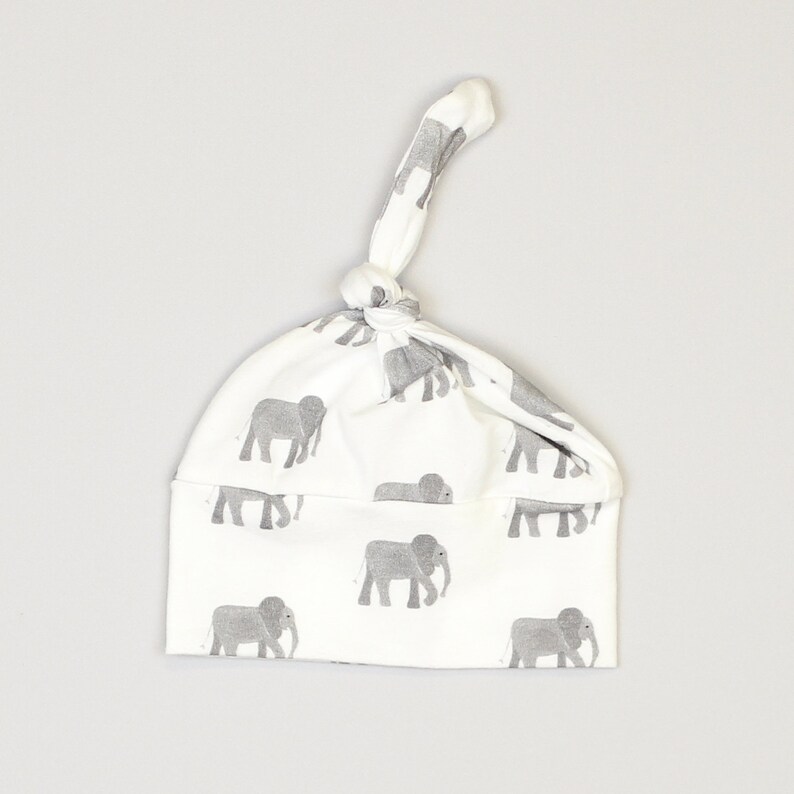 May include: White baby hat with a grey elephant print and a knot on top.