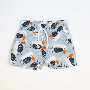 May include: Light blue swimming trunks with a white drawstring and a pattern of black and white birds with orange beaks.