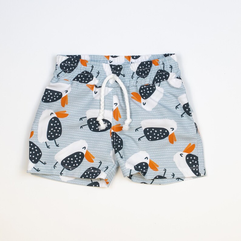 May include: Light blue swimming trunks with a white drawstring and a pattern of black and white birds with orange beaks.