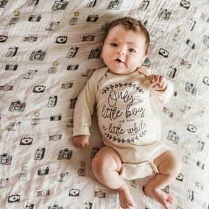 Pode incluir: Um beb&ecirc; vestindo um macac&atilde;o branco com texto preto que diz "Only a little boy - for such a little while". O macac&atilde;o &eacute; decorado com pequenos desenhos florais. O beb&ecirc; est&aacute; deitado em um cobertor branco com um padr&atilde;o de c&acirc;meras pretas.
