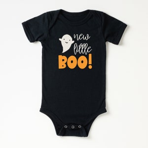 Pu&ograve; includere: Body nero per neonato con un fantasma bianco e testo arancione che dice "new little BOO!"