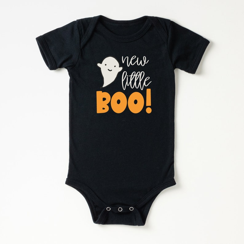 Pu&ograve; includere: Body nero per neonato con un fantasma bianco e testo arancione che dice "new little BOO!"