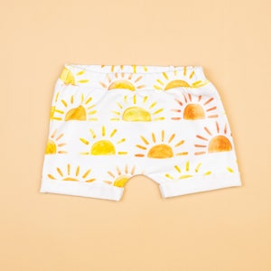 May include: White baby shorts with a yellow and orange watercolor sun print.