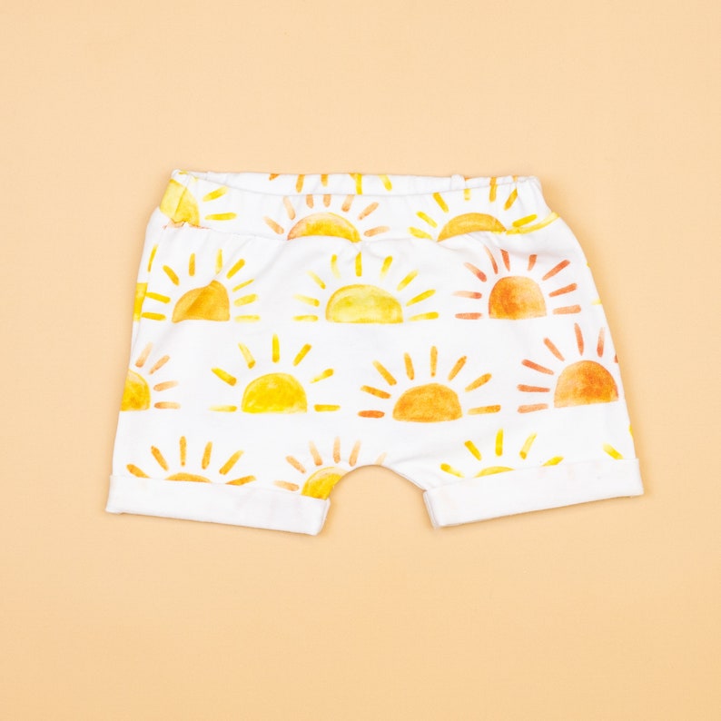 May include: White baby shorts with a yellow and orange watercolor sun print.