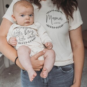 May include: A woman holding a baby wearing a white onesie with the text "Just a little boy with a little while" and a floral design. The woman is wearing a white t-shirt with the text "Mama -FOREVER- " and a floral design.