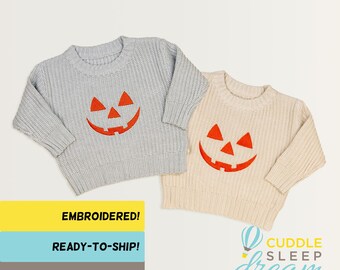 Puede incluir: Dos suéteres de punto con caras de calabaza bordadas. Los suéteres son grises y beige. El texto "EMBROIDERED!" está sobre un fondo amarillo, "READY-TO-SHIP!" está sobre un fondo azul y "ORDER BY OCT 24" está sobre un fondo gris. El texto "CUDDLE SLEEP dream" está sobre un fondo blanco con un gráfico de globo aerostático.