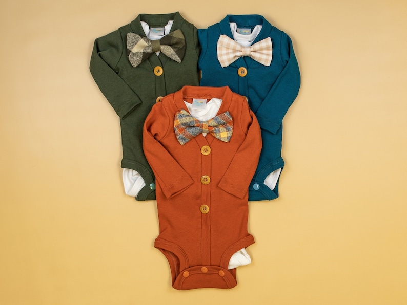 Op de afbeelding: Drie baby-rompers met lange mouwen en knoopsluiting. De rompers zijn in groen, turquoise en oranje. Elke romper heeft een andere gepatroneerde strik.