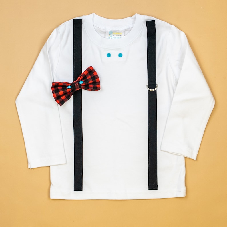May include: White long-sleeved shirt with black suspenders and a red and black bow tie. The shirt has two turquoise buttons on the front.