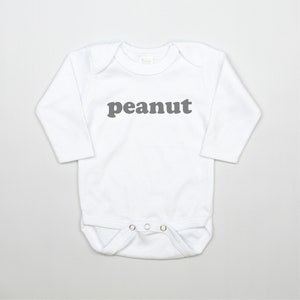 May include: White long-sleeve baby onesie with the word "peanut" printed in gray on the front.