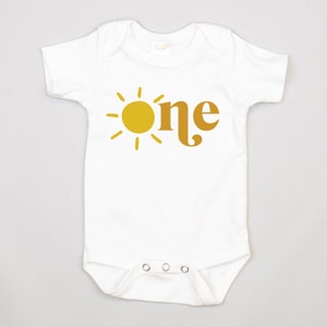 May include: White baby onesie with a yellow sun and the word "one" in brown.