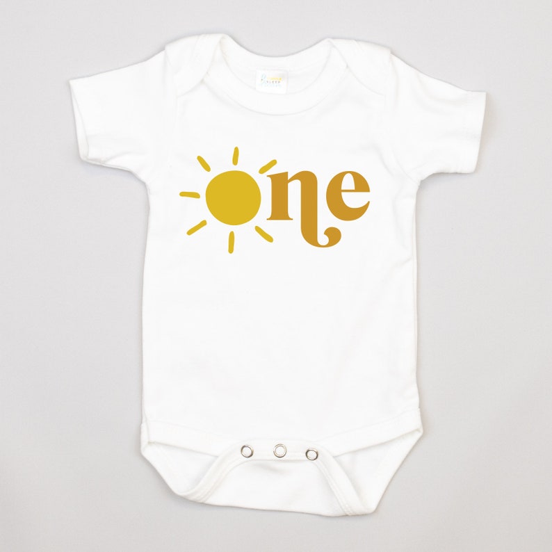 May include: White baby onesie with a yellow sun and the word "one" in brown.