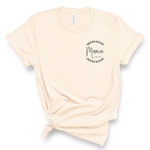 May include: A beige t-shirt with a black graphic that says "Mama Forever" inside a wreath of leaves.